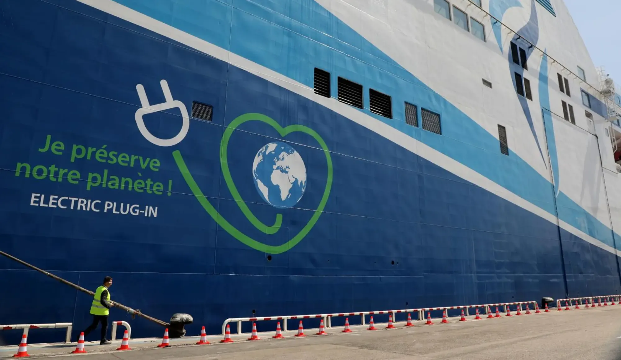 Navire à quai, avec la mention "Je préserve notre planète ! Electric plug-in" sur la coque
